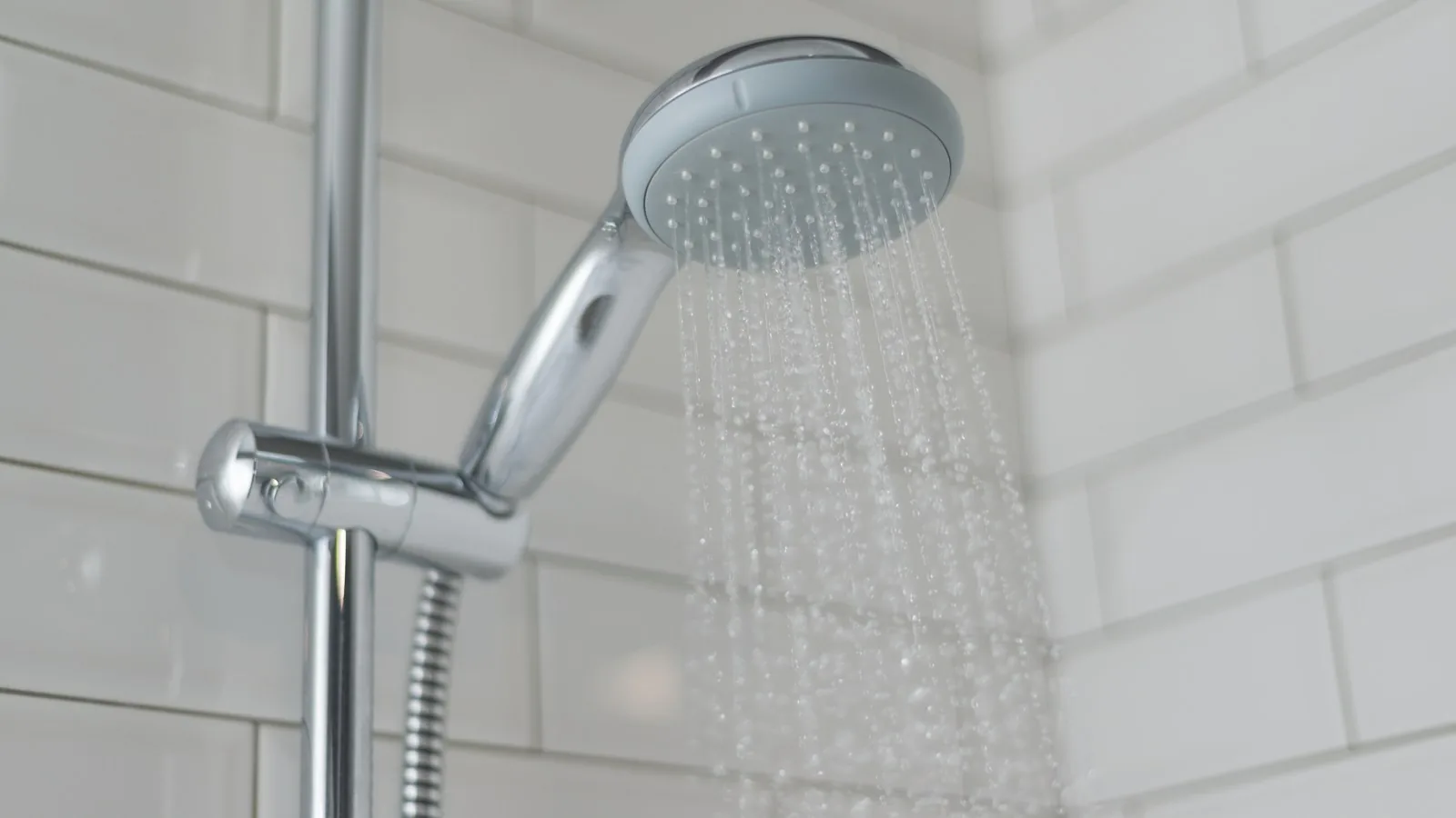 Chrome shower fixture mounted on white tiled bathroom wall